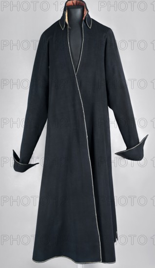 Kontusz, kontusz, men's clothing, Polish national costume. Kontusz of dark navy cloth with outlets in pink-crimson fabric patterned with small flowers and twigs. Fitted at the top, the skirts overlap at the bottom. Concealed front fastening with eight haberdashery buttons. Above the fastening, a triangular neckline culminates in a high, standing, turn-down collar. The back is cut in the classic style of a kontusz, with a pole and pleats at the sides. Pockets are trimmed in the folds and decoratively edged with gold cord, as are all garment edges. Long sleeves are set in and slit from the armpits to the elbows; cuffs are turned down. 1780s, Poland. Garment; length 118 cm, bottom circumference 318 cm., A long black coat displayed on a dress form against a light gray background, with a high collar showing a glimpse of orange-red lining, white piping along the front opening, collar edges, cuffs, and hem, long sleeves with turned-back pointed cuffs, and a smooth, slightly flared silhouette.