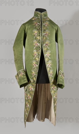 Habit à la française, Floral and plant motifs; embroidered green silk with small bouquets of flowers. Fitted at the top, widened at the back from the waist down with two slit pleats. Fastens at the front with hooks and eyes. Semicircularly cut lapels overlap at breast level and are cut off at the bottom. High, standing collar. Long sleeves set in at elbow height, cut in an arc, finished with wide, slightly protruding cuffs. Side pockets at hip level covered with trapezoidal flaps. Back with center seam; slits at hip level. Center back flaps meet without a pleat. Embroidery runs in a wide band around the edges, cuffs, pockets, collar, and back pleats. Decorative buttons sewn in threes on cuffs, under pocket flaps, two at top of back pleats, and in the pressed pleats. 1770s, Silesia; France place of creation. Garment; length 112 cm., A long green coat with a high collar displayed on a black form, decorated along the front edges, cuffs, and lower panels with embroidered floral motifs in c...