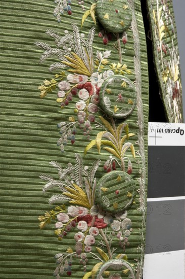 Habit à la française, repossession provenance; floral and plant motifs; fashion garment, men's clothing; embroidery; 18th century clothing; Habit of green silk embroidered with small bouquets of flowers. Fitted at the top, widened at the back from the waist down with two slit pleats. Fastens at the front with hooks and eyes. Semicircularly cut lapels overlap at breast level and are cut off at the bottom. High standing collar. Long sleeves set in at elbow height, cut in an arc, finished with wide slightly protruding cuffs. Side pockets at hip level covered with trapezoidal flaps. Back has a center seam. Slits at hip level. Center back flaps meet without a pleat. Embroidery runs in a wide band around the edges, cuffs, pockets, collar, and back pleats. Decorative buttons sewn in threes on cuffs, under pocket flaps, two at top of back pleats, and in the pressed pleats. 1770s; Silesia place of origin; France place of creation. Garment length 112 cm., A close-up of a textured green fabric wi...