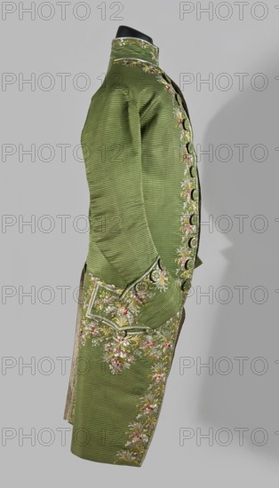 Habit à la française, repossession provenance; floral and plant motifs; embroidery; 18th century clothing. Habit of green silk embroidered with motifs of small bouquets of flowers. Fitted at the top, widened at the back from the waist down with two slit pleats. Fastens at the front with hooks and eyes. Semicircularly cut lapels overlap at breast level and are cut off at the bottom. High standing collar. Long sleeves set in at elbow height, cut in an arc, finished with wide, slightly protruding cuffs. Side pockets at hip level covered with trapezoidal flaps. Back with a center seam. Slits at hip level. Center back flaps meet without a pleat. Embroidery runs in a wide band around the edges, cuffs, pockets, collar, and back pleats. Decorative buttons sewn in threes on the cuffs, under the pocket flaps, two at the top of the back pleats, and in the pressed pleats. 1770s, Silesia place of origin and France place of creation; garment; length 112 cm., A side view of a long green coat displaye...