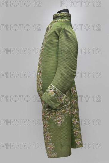 Habit à la française, Repossession provenance. Floral and plant motifs; embroidery. 18th century 1770s. Habit of green silk embroidered with small bouquets of flowers. Fitted at the top, widened at the back from the waist down with two slit pleats. Fastens at the front with hooks and eyes. Semicircularly cut lapels overlap at breast level and are cut off at the bottom. High standing collar. Long sleeves set in at elbow height, cut in an arc, finished with wide slightly protruding cuffs. Side pockets at hip level covered with trapezoidal flaps. Back cut with a center seam; slits at hip level. Center back flaps meet without a pleat. Embroidery runs in a wide band around the edges, cuffs, pockets, collar, and back pleats. Decorative buttons sewn in groups of three on the cuffs, under pocket flaps, two at the top of the back pleats, and in the pressed pleats. Silesia place of origin and France place of creation. Garment; length 112 cm., A side view of a long tailored coat displayed on a bl...
