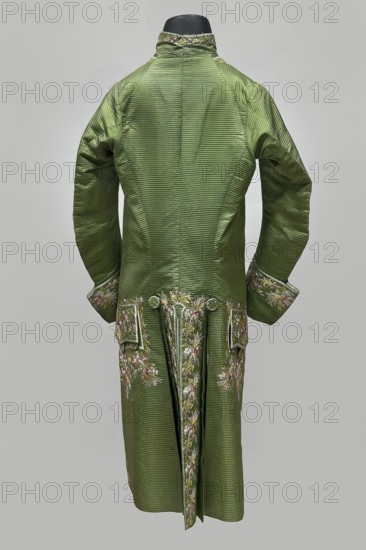Habit à la française, repossession provenance; floral and plant motifs; fashion garment men's clothing, embroidery; 18th century 1770s; Habit of green silk embroidered with motifs of small bouquets of flowers. Fitted at the top, widened at the back from the waist down with two slit pleats. Fastens at the front with hooks and eyes. Semicircularly cut lapels overlap at breast level and are cut off at the bottom. High, standing collar. Long sleeves set in at elbow height, cut in an arc, finished with wide, slightly protruding cuffs. Side hip pockets covered with trapezoidal flaps. Back cut with a center seam. Slits at hip level. Center back flaps meet without a pleat. Embroidery runs in a wide band around the edges, cuffs, pockets, collar, and back pleats. Decorative buttons sewn in threes on cuffs, under pocket flaps, two at the top of the back pleats, and in the pressed pleats. Origin: Silesia; creation: France; garment length 112 cm., A long green coat displayed from the back on a blac...