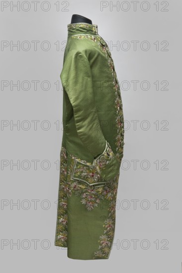 Habit à la française, repossession provenance; floral and plant motifs; fashion, men's clothing; embroidery; 18th century clothing. Habit of green silk embroidered with motifs of small bouquets of flowers. Fitted at the top, widened at the back from the waist down with two slit pleats. Fastens at the front with hooks and eyes. Semicircularly cut lapels overlap at breast level and are cut off at the bottom. High, standing collar. Long sleeves set in at elbow height, cut in an arc, finished with wide, slightly protruding cuffs. Side pockets at hip level covered with trapezoidal flaps. Back cut with a center seam. Slits at hip level. Center back flaps meet without a pleat. Embroidery runs in a wide band around the edges, cuffs, pockets, collar, and back pleats. Decorative buttons sewn in threes on the cuffs, under the pocket flaps, two at the top of the back pleats, and in the pressed pleats. 1770s, Silesia; France place of creation. Garment, length 112 cm., A side view of a long coat dis...