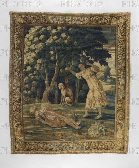 Tapestry, Mythological scene: in the center foreground Endymion lies on the ground with a staff beside him; above him stands Diana with raised arms and a dog. Background: a forest and, on the right, a hilly landscape. Border with scrolls of flowers and acanthus leaves; masks in the upper corners. Motifs: flowers, leaves, floral ornaments, trees, landscapes. Colors: brown, beige, and green. 1st half of the 18th century, Europe. Textiles; height 312 cm, width 263 cm., A woven rectangular tapestry with a decorative border in shades of gold, brown, and muted green surrounds a central scene rendered in deep blue, green, beige, and tan tones. The central scene shows a wooded landscape with several trees bearing pale yellowish foliage against a dark blue-green background. In the foreground, a figure in a flowing beige dress stands with arms raised and fabric draping around the legs, while another figure reclines on the ground wearing similar beige clothing. A seated dog with tan and brown col...