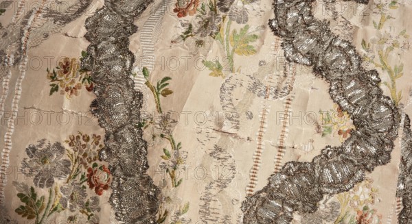 Robe à la française robe à paniers à coudes, two-piece, pink grosgrain with swirling silver lamellar brocade, silver lace ribbons and bouquets of flowers; c. 1764. Worn on an oval corselet. a Outer dress manteau open at the front with pleated train at the back. Bodice stiffened with 22 long bonings, laced at front and back under the pleats. Elbow-length curved sleeves finished with double flounces trimmed with silver lace. Constructed from eight panels; quadruple pleats at the back preserve full fabric width, with cuts and fittings only at the front. Silver lace appliqué on the edges echoes the wavy brocade pattern. b Apron of same fabric, hemmed with a wide ruffle and matching silver lace appliqués repeating the wavy brocade motif. Materials/measurements: fabric height 37 cm x width 27 cm; fabric width 55.5 cm. Garment length 167 cm; width at bottom of manteau 430 cm. Origin: France fabric; place of use: Poland., Tags: lace ornaments; floral bouquets; ribbon ornament; women's 18th-cen...