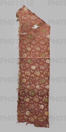 Fabric fragment, 17th century, Italy, warp-woven satin background with pale red silk warp and two alternating wefts white and yellow creating the pattern using the lisère technique; brooching wefts in green and beige; high fabric tightness. SATIN WITH A TWO-COLOR WEFT, LISÉRE. Construction: floating runs in diagonal, fairly wide bands. Pattern report length 29 x width 17.5 cm. Floral motifs in three types arranged at close intervals: two kinds of carnations rows facing left or right, tulips with drooping calyxes, and roses with spread petals, with smaller flower projections scattered between them facing in different directions. Colors of flowers and elements vary — white and yellow stems and leaves, green and beige calyxes. Fragments of silk patterned fabric, height 112 cm, width 28.5 cm., A long, narrow piece of worn fabric with an irregular top edge and frayed sides, patterned with a repeating floral motif; the fabric's base color is a muted reddish-brown with floral elements in shad...