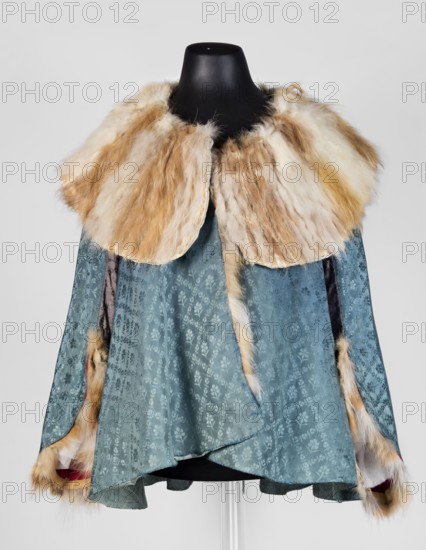 Jubka, geometric ornaments, caftans, clothing, women's clothing, fashion, women's fashion. Long women's caftan, hip-length, narrow in the shoulders, flared at the bottom. Large turn-down collar entirely trimmed with fur two types of fur decoratively connected in narrow bands. Long set-in sleeves, narrow at the top, flared at the bottom, lined with white sheepskin with strongly twisted fleece. Late 18th century, Poland. Clothing. Length 63 cm, circumference 292 cm at the bottom., A garment displayed on a black mannequin torso features a wide collar trimmed with long, fluffy fur in shades of cream, beige, and light brown, with a narrow fur tail hanging down the front; the main body of the piece is made of a patterned, slightly textured fabric in blue-green with a subtle floral motif, and the interior and sleeve edges show accents of darker fabric and glimpses of red and white beneath fur-trimmed openings.