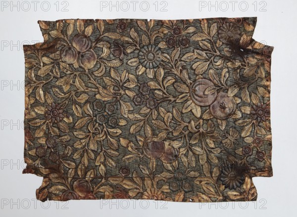 Fragment of cordovan leather, cordovan leather, flowers, fruit, butterflies, Scheele, Stanislaw fl. ca. 1919, furniture upholstery, Seat or backrest of a chair made of embossed, painted, and gilded leather. The entire surface of the leather is filled with floral and fruit decoration. Leafy branches with small flowers and fruit, on and between which are placed small insects butterflies and flies. The background of the entire decoration is textured with a fine mesh of lines enclosed in triangles. 17th/18th century, Europe, varia. Height 32 cm, width 44 cm., A rectangular piece of patterned material with irregular torn edges, showing a dense floral and foliage design in shades of gold, brown, dark green, and muted reddish tones on a textured dark background; the surface features a repeating pattern of leaves, stylized flowers, and round fruit-like shapes, with some areas appearing worn or darker and a few places showing small holes or frayed edges.