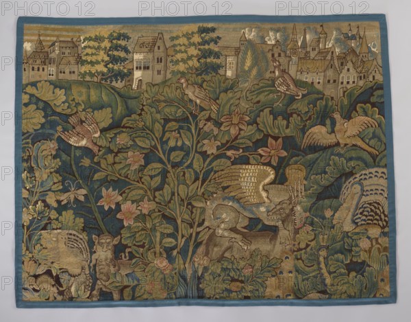 Tapestry-verdure, verdure with flowers and leaves, floral ornaments, 17th century, Flanders, fabric, height 194 cm, width 240 cm, A woven textile with a blue border shows a detailed scene of foliage, flowers, birds, and mythical creatures in a palette of blue, green, gold, brown, and muted pink. At the top, a row of stylized buildings sits behind a band of trees in green and gold. The central area is dominated by a large plant with many green leaves and pink flowers growing against a deep blue background, with several birds perched among the branches and flying, their plumage rendered in gold, brown, and pale pink. Around the lower and side areas are various animals and fantastical beasts, including a winged creature with gold wings, a horned head, and a lion-like body in shades of brown and gold, as well as other creatures with patterned tails and feathered forms in blue, gold, and brown tones. The composition is richly filled with layered leaves, curling vines, and floral motifs in g...
