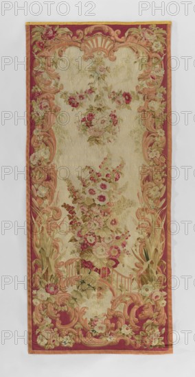 Figural tapestry, flowers, leaves, floral ornaments, garlands. In the center, a large bouquet of flowers sits on a bridge with a fanciful balustrade, above which is a floral garland with a hanging bouquet; at the bottom are volutes and flowers. The border is composed of volutes, rocailles, and flowers, and around the bridge are tall reeds. Colors: beige, pink, light green, and red. Circa mid-18th century. Fabric. Height 302 cm, width 123 cm., A rectangular textile panel with an ornate floral tapestry design featuring a central field in a light beige color surrounded by a wide decorative border in deep red and muted orange; the tapestry shows a vertical arrangement of floral bouquets and garlands in shades of pink, rose, cream, pale yellow, and green with leafy accents in various greens and olive tones; scrolling acanthus-like motifs in warm peach and coral frame the central area and are repeated along the sides and corners, integrating clusters of flowers in pale cream, pink, and red; ...