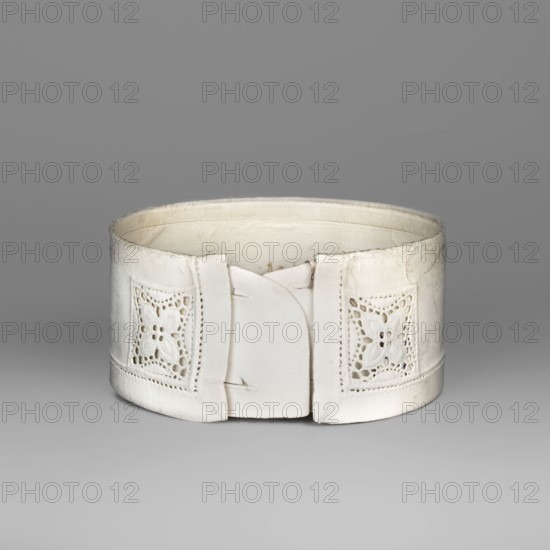 Women's collar, made of thin white linen, stiffened, decorated with openwork embroidery. Edges on the front are decorated with rosettes in the form of a square. White embroidery. 19th/20th century, Poland. Clothing accessory; height 5.5 cm, width 40 cm. Function: women's fashion accessory collar., A white cylindrical fabric object with a cutwork floral motif on each side and a plain central front panel, shown against a smooth gray background; the fabric appears slightly worn with subtle shadows and highlights in shades of white, off-white, cream, and gray.