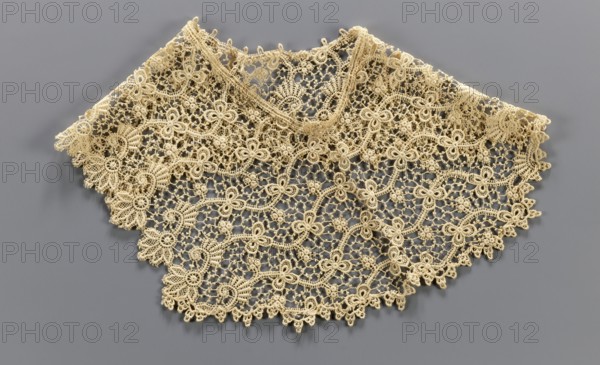 Pair of cuffs, ca. 19th century, Europe; lace cuffs with plant ornament decoration; fashion accessory; clothing; circumference 43 cm., A delicate beige lace collar with an openwork floral and scroll pattern is displayed flat against a smooth gray background, showing a scalloped lower edge of interconnected motifs and a rounded top opening, with intricate loops, knot-like clusters, and leaf-shaped elements creating a repeating ornamental design.