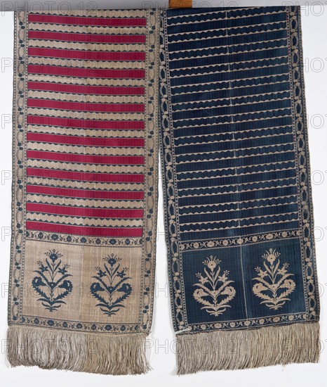 Kontusz belt, flower bushes ornament, double-sided belt, plant ornaments, Polish costume, Poland culture, half-solid belt, kontusz belt, bipartite heads with an ornament of stylized flower bouquets, plain belts and belts with serrated ribbon, wreath edging. Colors: gold, silver, blue, black. 2nd half of the 18th century, Lyon. Clothing accessory, national costume. Length 360 cm, width 35 cm., A pair of long woven textiles displayed side by side, each with horizontal banding and decorative borders; the left textile shows alternating deep red and beige wavy stripes with a beige border patterned in blue, and a lower panel featuring a beige field with two stylized floral motifs in blue and a fringe of beige threads, while the right textile displays alternating dark blue and beige wavy stripes with a matching beige border patterned in blue, and a lower panel with a dark blue field containing two stylized floral motifs in beige and a fringe of beige threads.