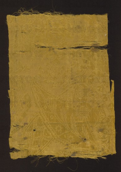 Fabric fragment, patterned silk damask, early 18th century, France. Fragment of yellow semi-silk damask with floral-fantasy motifs. Background is warp-covered satin with a plain-weave ornament. Decorated with stylized large leaves with frayed edges, small heart-shaped leaves, small leaves and flowers, blades of grass, small fruit, details evoking Far Eastern architecture, and openwork lace-like elements in a bizarre style. Background and pattern are yellow Jaune d'or group according to Newton's palette. Fragment size: height 34 cm, width 23.5 cm., A rectangular piece of woven fabric with frayed edges and loose threads, showing a subtle raised pattern across its surface; the fabric is primarily a golden yellow color set against a dark background, with areas of darker discoloration and small worn holes, and a few horizontal slits and tears near the top and bottom.