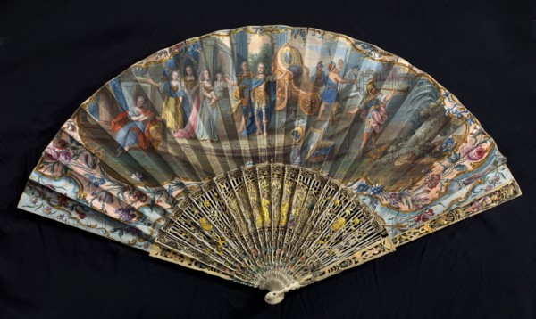 Fan, double-sided fan, paper painted with gouache and gold dust. On the obverse, a scene of two knights dressed in Roman costume welcomed by trumpeters; women in flowing robes greet them, one carrying a child. Composition surrounded by a margin of leaves and flowers; decorated in light pastel colors and gilded ornament. On the reverse, children playing in a meadow among trees and flowers. Feathers cut from ivory, openwork, painted with oil and inlaid with gilded tin foil. Central cartouche with a figural representation against palace and garden architecture. 2nd half of the 18th century, France. Height 40.4 cm., A decorative folding fan displayed open against a dark background shows a painted scene across the leaf with a group of figures in period clothing and classical architectural and landscape elements, framed by floral ornamental borders; colors visible include blue, pink, yellow, gold, green, red, brown, cream, and black. The fan sticks and guards feature intricate openwork carvi...