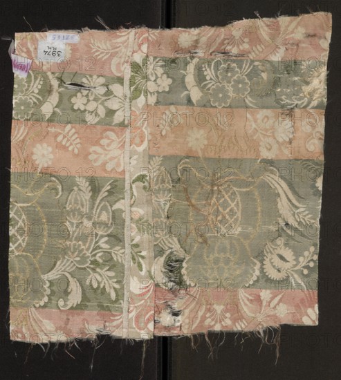Fabric fragment. Cream silk damask fabric, embroidered and brocaded with colorful threads. Promoting pattern threads: green, light and dark salmon. Brooching thread: gold. Pale cream satin background with weft weave coverings, embroidering, and brocade. Fantastical floral decoration: stylized pomegranates pineapples placed on a winding stem, surrounded by sprigs of smaller flowers; small twigs and leaves of the damask sub-report complement larger motifs brocaded with gold threads. Fabric sewn from two pieces. Composition of the report motifs based on mirror symmetry. Weave: satin weave with warp coverage; pattern creating a sub-report in plain weave; colorful pattern promoted in zones; promoting threads tied in a twill weave introduced two at a time in the interlacing. Date: 1710–1715. Place of origin: France. Materials/technique: silk damask, embroidery, brocade, gold thread. Dimensions: height 33 cm, width 33.5 cm., A worn rectangular fabric sample with alternating horizontal bands o...