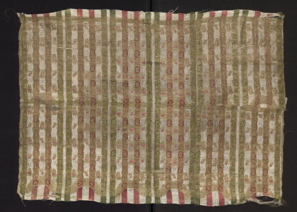 Fragment of silk fabric with fine stripes and a stylized plant ornament. Predominant colors: dirty-white background with red, green and gold ornament. Closed composition suggests it may be a fragment of patterned fabric used for tapestries or as a border on larger decorative textiles. Gold-plated threads. Fragments of a larger textile object; patterned silk fabric, early 18th century, Europe . Width 41 cm; overall height 60.5 cm, width 45 cm; report width 10 cm. Thread density per 1 cm: 18 white linen, 18 gold on a yellow soul with a loose S braid; warp density 46 per 1 cm; edge width 0.4 cm 4 linen warp threads on the edge. Warp satin background 1/5., A rectangular woven textile displayed flat against a dark background, showing a repeated vertical striped pattern with alternating wider pale beige bands and narrower greenish-olive bands, with additional thin vertical accents in cream, pink, and muted red. The fabric surface has a repeating ornamental motif within the stripes consisting...