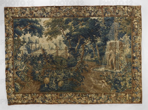 Tapestry - verdure, Flowers, floral ornaments, dogs, deer, tapestries, interior furnishings, park scenes, decorative tapestries, park scenes with architecture, interior decorations, animals, fountains, borders, trees, garden scenes, landscape scenes, parks, park sculptures, gardens. On the right, a fountain with two piled goblets, one supported by Atlas; in front of the fountain a dog and a deer. In the center foreground, a bush with pumpkin fruit. In the background on the left, garden architecture; in the center and right, trees. Border with floral motifs, fruit, and musical instruments. Colors: green, blue, brown, ochre, yellow. Late 17th century, Flanders. Fabric. Height 415 cm, width 297 cm., A woven scene shows a wooded landscape with a group of large trees in shades of deep blue, green, and brown, with areas of beige and tan suggesting sky or distant ground. In the right foreground a sculpted fountain with cascading streams of pale blue and white water stands on a circular basin,...
