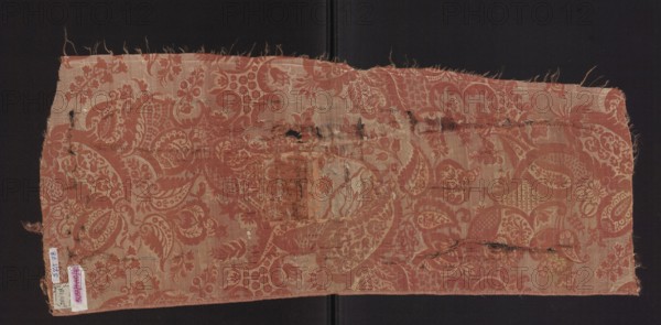 Fabric fragment, fragments of a larger textile object, patterned silk fabrics, pale red pink lampas with a white patterned weft. A unilateral two-tone damask: light red/pink warp satin background, overlays in plain and liseré weaves with a white weft tied in a weft weft-faced weave; reverse in plain weave. Repeat composed of small flowers, fanciful leaves, and miniature lace motifs forming an ornament on the leaves; motifs typical of bizarre fabrics inspired by lace. Fragment no. SZT 79 likely part of the same fabric. Weave structure details: background in warp satin pink warp; subreport areas in plain weave pink warp, pink weft; white weft areas in weft weave; reverse plain weave. Colors: pink background with white decorative pattern. Hem width: 0.4 cm. Repeat report dimensions: length 64.5 cm; width 24.5 cm. Overall dimensions: height 73 cm; width 31 cm. Date: early 18th century, France., A rectangular piece of woven fabric with frayed edges lies flat against a dark background, showi...