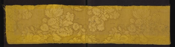 Fabric fragment, silk fabrics, unknown provenance; fragments of patterned silk damask with floral bouquet motifs on a zigzag-filled background. Background weave: warp satin 7/1; pattern: gros de Tours. Preserved selvedge selvedge width 0.8 cm; selvedge threads: white, yellow, green. Motif height 47 cm. Reported overall fragment dimensions: height 101 cm, width 20 cm. Ca. mid-18th century, France attributed., A long horizontal textile strip with a floral damask pattern laid flat against a dark background, showing a repeating design of stylized flowers, leaves, and scroll-like foliage woven into the fabric; the textile has a slightly worn edge on one side and a subtle central fold line, with visible weave textures and areas of light variation across the surface; the dominant color is yellow with lighter and deeper yellow tones creating the pattern, and the background behind the strip appears black.