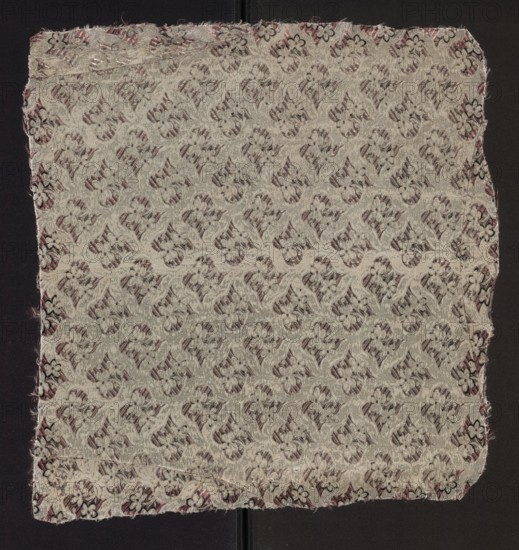 Fabric fragment, fabrics, fragments of silk patterned fabric with floral motifs. Dimensions of the fragment: 7.5 x 7 report and overall height 51 cm, width 48 cm. Colors: white background with motifs in pale pink, plum, and black. 2nd half of the 18th century, France., A square piece of woven fabric with a repeating floral and curving motif covering the surface, displayed on a dark background. The fabric shows a textured, raised pattern in pale beige or off-white threads against a muted darker backing that appears dusky purple or brown. Along the edges there is a border with small floral shapes and frayed threads, showing hints of darker purple and black. The woven pattern creates a subtle contrast between the light raised design and the deeper, shadowed areas, and the fabric edges are slightly irregular with loose fibers visible.