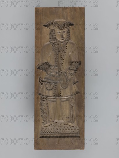 Double-sided gingerbread mould. Side A: image of a bachelor; Side B: baby in swaddling clothes., woodcarver or gingerbread maker. Double-sided, rectangular mould. One side: man in a long wig and tricorn hat, dressed in costume probably dating from turn of 17th–18th centuries—justaucorps with decorative cuffs, culottes and stockings, high-heeled shoes; at his feet decorative flower and geometric motifs and the date 1827. Other side: baby in swaddling clothes richly decorated with geometric and plant ornament. Inscription on the edge: FW FIEBIGER. a. BAUTZEN. 17 signature of the manufacturer and beginning of the date. Silesia Prussia; 1827; Bautzen. Material: form. Height 64 cm; width 22.5 cm; depth 4.3 cm., A carved wooden panel depicting a full-length figure of a person in period dress, shown standing and facing forward, with a tricorn-style hat, long curled hair, and a coat with decorative buttons and patterned cuffs; the figure holds an object at the waist and wears a skirt-like garm...