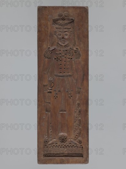 Double-sided gingerbread mould. Side A: image of a soldier; Side B: baby in swaddling clothes., woodcarver or gingerbread maker. Gingerbread mould, decorative art; double-sided, rectangular mould. One side: figure of a soldier in a parade uniform from the beginning of the 19th century, wearing a high shako decorated with a tassel, epaulettes and decorative sleeves, an order pinned on the chest, a sabre with a decorative tassel at the leg; bottom geometric and plant decoration. Other side: baby in swaddling clothes richly decorated with geometric and plant ornament. Letter engraved on the edge: B initial of the woodcarver or gingerbread maker. 19th century, Silesia Province 1742–1918. Dimensions: height 35.3 cm, width 11.6 cm, depth 3.5 cm. Materials: wood gingerbread form. Subjects: male figures, historical costumes, plant ornaments, military uniforms, folk motifs, folk customs., A tall rectangular wooden panel carved in a single brown wood tone shows a stylized standing human figure i...