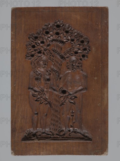 A single-sided gingerbread mold with the image of Adam and Eve in paradise. A single-sided, rectangular mold with a representation of naked figures of Adam and Eve standing under the Tree of Knowledge bearing numerous fruits; Eve gives Adam an apple and a snake is wrapped around the tree. Gingerbread; decorative folk motifs; figurative, biblical and religious iconography. 19th century, Province of Silesia 1742–1918. Mold. Height 20.5 cm, width 13.8 cm, depth 2.5 cm., A carved wooden panel showing a relief of two human figures standing on either side of a stylized tree with a textured trunk and a canopy of leaves with round openings; the figures appear nude with carved hair and facial features, the left figure having long wavy hair and the right figure having a beard, and both holding or touching the tree; the lower section shows carved ground decoration and plant forms; the wood shows a warm brown color with darker carved recesses and a few lighter scuffs and worn edges, and the backgr...