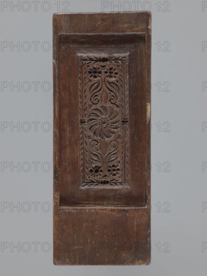 Double-sided gingerbread mould. Obverse: rectangular floral and geometric ornament; a rectangular decorative motif containing a rosette and stylised plants. Reverse: image of the Archangel Michael in a long patterned robe decorated with a plant twig motif, holding scales in his right hand and a sword in his left; at the feet of the figure a geometric-plant ornament. Date engraved on the edge: 1806 with the letter S against the background of an anchor mark of the woodcarver or gingerbread maker. Maker: woodcarver or gingerbread, Material/technique: bas-relief. Subject/themes: gingerbread, decorative and folk art, angels, Archangel Michael, Christian religious motifs, floral ornaments, figurative scenes, folk-style decorations. Origin/provenance: Silesia Province of Silesia, 1742–1918, circa 1806. Dimensions: height 11.6 cm, width 30.5 cm, depth 3 cm., A rectangular wooden panel in shades of brown with a darker brown carved central panel featuring floral and foliate motifs, including a s...