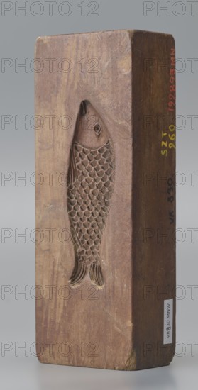 Double-sided gingerbread mould. Side A: figure of a lady in a decorative, pleated dress from the beginning of the 19th century, holding a bouquet of roses. Side B: stylised fish covered with scales shown in profile. Rectangular wooden mould, double-sided. On the edge an engraved date 1808 with the letter S against the background of an anchor mark of the woodcarver or gingerbread maker. Materials: wood; function: gingerbread mould. Subject motifs: female figure in rich dress, flowers, fish, zoomorphic and folk motifs; style: decorative/fairly folk. Dimensions: height 19.8 cm, width 7.3 cm, depth 4 cm. Origin: Silesia Province of Silesia; 1742–1918, dated 1808. Maker: unknown woodcarver or gingerbread maker., A rectangular block of wood shown upright with a carved recessed fish motif on its front face, the wood displaying grain patterns and worn areas; the carved fish has a head, eye, detailed overlapping scale texture along its body, and a tail with carved fin lines, and there are areas...