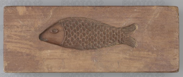 Double-sided gingerbread mould. Side A: figure of a lady in a decorative, pleated dress from the beginning of the 19th century, holding a bouquet of roses. Side B: stylised fish covered with scales shown in profile. Rectangular wooden mould, double-sided, with an edge engraving: 1808 with the letter S against the background of an anchor the maker's mark. Woodcarver or gingerbread, Gingerbread mould, unknown origin; decorative folk motifs, female figures in rich historical costumes, zoomorphic motifs; Silesia Province of Silesia, 1808. Height 19.8 cm, width 7.3 cm, depth 4 cm., A rectangular wooden block with a carved fish in relief occupying the center; the fish has a rounded head, a carved eye, a textured body of overlapping scales, and a forked tail with carved lines, all carved into the same wood surface. The wood shows a natural grain with worn and slightly discolored areas and small surface scratches. The visible colors are shades of brown with some lighter beige tones and subtle ...
