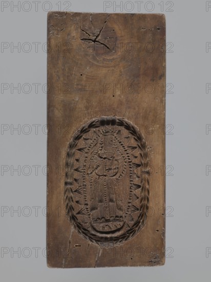 Double-sided gingerbread mould. Obverse: image of Madonna and Child. Reverse: small image of Madonna in oval. Double-sided, rectangular form; on one side a figure of Madonna and Child, with a crown on her head, in a long patterned robe decorated with various geometric and plant motifs, the Madonna holds the Child in her left hand and a sword in her right; the other side: a smaller figure of the Madonna in an oval, surrounded by rays, the whole surrounded by a laurel wreath. Gingerbread mould; gingerbread; decorative art; religious motifs; Madonna and Child iconography; crown iconographic; sword iconographic; wreaths; female figures in rich dresses; folk motifs. 19th century, Province of Silesia 1742–1918. Dimensions: height 25.8 cm, width 12 cm, depth 4.5 cm., A rectangular wooden board with a carved oval design near the lower half, the wood showing a brown tone with lighter and darker variations, cracks, small holes, and surface scratches; the carved oval contains a central standing f...