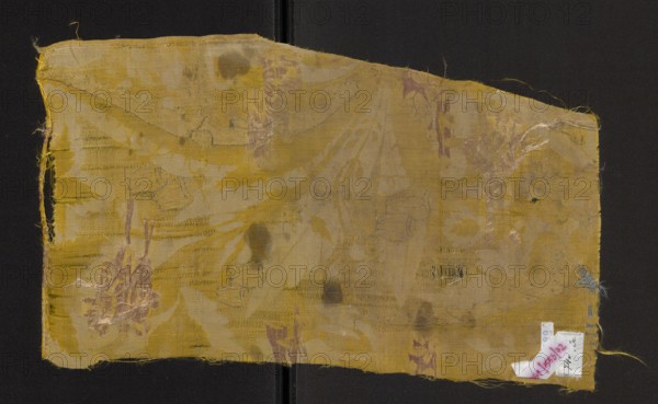 Fabric fragment, fragments of silk patterned fabrics, yellow silk damask, embroidered and brocaded with fanciful plant decoration. Damask substructure, satin with warp and grosgrain; decoration embellished with white weft and colored wefts. Elongated, frayed leaves form a background for smaller fanciful flowers brocaded with colored threads. Colors: white and yellow background. Embroidery with colored threads: sea green, light pink, dark pink, gold metallic thread. Edge width selvage: 0.3 cm; selvage made of thicker yellow threads. Early 18th century, Europe. Fabrics, height 44 cm, width 25 cm., A rectangular piece of worn fabric with frayed edges laid flat against a dark background, showing a faded pattern and several areas of damage and loose threads; the fabric is primarily yellow with lighter beige areas and small touches of purple and blue in places, and there are darker brownish stains and irregular discolored spots across the surface.