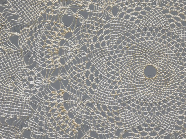 Napkin, napkin, gift, lace, lace napkin, white, round, large triangular teeth along the edge, concentric and radial geometric ornament, 20th century, Poland, fabric, lace, diameter 33 cm, A delicate crocheted lace fabric with an intricate circular and floral pattern in off-white and cream tones laid over a medium gray background, showing a group of openwork loops, scalloped edges, and radiating concentric rings with a few larger circular holes and several smaller mesh-like areas formed by fine threads.