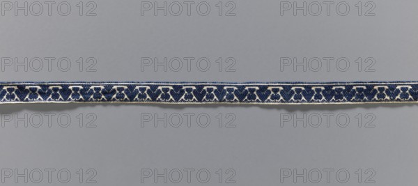 Gallon, galloons haberdashery, origin unknown, plant ornaments, 19th century, Europe, fabric haberdashery, width 1.3 cm, length 49.5 cm, A narrow woven band stretches horizontally across a plain neutral background, showing a repeating geometric pattern in dark blue and lighter blue on an off-white base; the band has a textured, slightly raised surface and bordered edges that contrast subtly with the background, and a faint shadow runs beneath it.