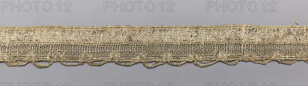 Gallon-lace, galloons haberdashery, origin unknown, haberdashery, 18th/19th century, France, fabric, width 2.7 cm, length 73 cm, A narrow horizontal textile strip lies against a smooth background, showing an open, loosely woven structure with a decorative lower edge of looped scallops; the material has a metallic sheen and appears gold in color, with the background visible through the mesh in gray tones, and some slight variations where threads catch the light giving brighter and darker golden highlights.