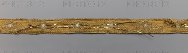 Gallon, gallons haberdashery, origin unknown, plant ornaments, 18th century, Poland, Drzewica, fabric haberdashery, width 1.4 cm, length 40 cm, A narrow woven trim lies horizontally against a plain background, showing a textured band with a slightly irregular edge and a linear pattern along its length; the trim features loose metallic strands and thin ribbon-like elements intertwined on its surface, creating a mix of straight and curving lines and occasional small knotted areas; visible colors include gold, yellow, silver, and gray, with the background appearing light gray.