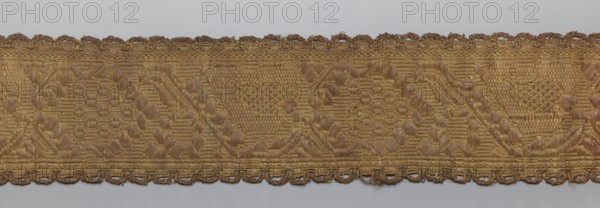 Gallon, gallons haberdashery, origin unknown, plant ornaments, 19th century, Lithuania, fabric haberdashery, width 8.5 cm, length 99 cm, A horizontal strip of woven fabric with a repeating textured geometric and floral-like pattern in shades of gold and brown, featuring a scalloped embroidered edge along both the top and bottom; the weave shows alternating raised and flat areas creating a subtle contrast in sheen, with visible threads in gold, bronze, and darker brown tones against a neutral light gray background.