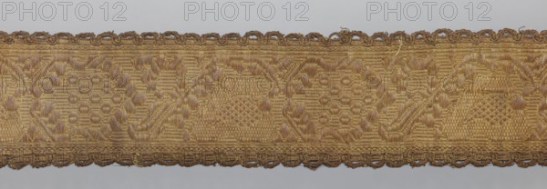 Gallon, gallons haberdashery, origin unknown, plant ornaments, 19th century, Lithuania, fabric haberdashery, width 8.5 cm, length 99 cm, A horizontal woven trim with a textured pattern in shades of gold and brown, showing a repeating ornamental motif and a scalloped braided edge along both long sides, with visible woven threads and slight irregularities in the fabric.