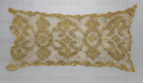 Fragment of lace, lace, 17th/18th century, Belgium, fabric, lace, width 34 cm, length 67 cm, A rectangular lace textile displayed flat against a pale gray background, with an open mesh ground and an ornate repeating floral and geometric pattern worked in a metallic golden thread; the lace has scalloped irregular edges and a delicate net-like structure, with several larger circular and diamond-shaped motifs interconnected by smaller curving elements, and the overall palette shows gold against light gray.