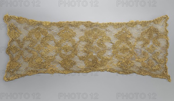 Fragment of lace, lace, 17th/18th century, Belgium, fabric, lace, width 31 cm, length 76 cm, A rectangular piece of openwork fabric displayed against a neutral backdrop showing a delicate net-like ground with raised ornate motifs, scalloped edges, and irregular outlines. The fabric has a metallic sheen and appears textured with sections that are denser and more raised than the surrounding mesh. The visible colors are gold in the fabric and a soft gray in the background.