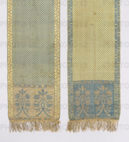 Kontusz belt, Aleksander Unrug Manufactory Kobylka; belt manufacturer; 1781–1787. Solid, double-sided kontusz belt; length 354 cm, width 28 cm. Bipartite heads with motif of two rooted and connected twigs with flowers and leaves forming a bouquet. Center with carp-scale pattern. Longitudinal border of winding tendrils: leaves with flowers and small-leaf tendrils; crosswise border of projecting flowers with leaves; borders also include a snake motif. Sewn-on gold fringe metal and cotton. Ornament: heads—two floral motifs of two branches topped with a common trefoil; center—carp scale motif; borders—vertical and horizontal floral tendril motif intertwined with a wavy ribbon. Colors: gold background of heads and horizontal borders with blue ornament; straw background of vertical borders with gold and blue ornament; blue background in center with straw-colored scale pattern. Reverse right. Signed in the heads: KOB:/YLKI. Materials and technique: silk and gold thread; thread density approx....