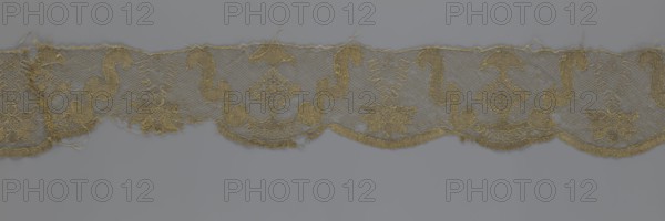 Lace fragment, lace strip finished with flat arched teeth on one side and straight on the other; in the divisions corresponding to the teeth, an alternating flower calyx and rhombus motif are placed, separated by parenthetical geometric forms. 18th century, France; fabric; width 17.5 cm, length 308 cm., A length of delicate lace trim displayed against a neutral background, featuring a repeating scalloped lower edge and a straight upper edge; the lace shows a mesh ground with ornate embroidered motifs including floral shapes, stylized scrolls, and diamond-like elements; the fabric appears slightly frayed in places with loose threads and some irregularities along the edges; visible colors include gold in the embroidery and a muted grayish background.