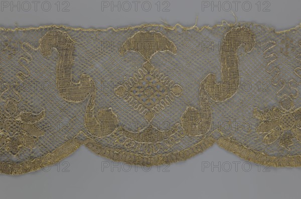Lace fragment, lace strip finished with flat arched teeth on one side and straight on the other. In the divisions corresponding to the teeth are alternating flower calyx and rhombus motifs, separated by parenthetical geometric forms. 18th century, France. Materials: lace, fabric. Width 17.5 cm, length 308 cm., A strip of delicate openwork fabric with an intricate lace pattern in gold thread set against a gray background, showing a repeating scalloped lower edge with decorative curved and floral motifs, a diamond-shaped central lattice motif, fine netting between the embroidered elements, and a few loose threads along the top edge.