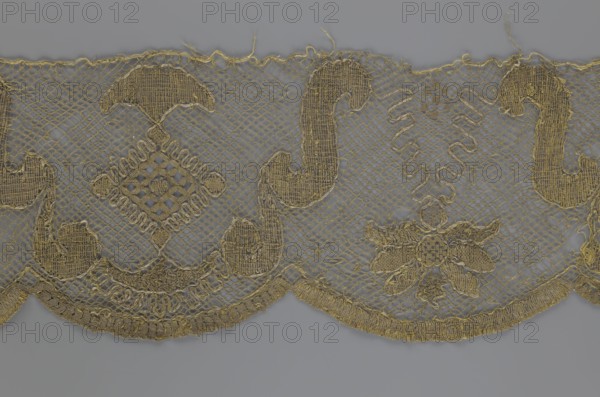 Lace fragment, lace strip finished with flat arched teeth on one side and straight on the other; in the divisions corresponding to the teeth, an alternating flower calyx and a rhombus motif are placed, separated by parenthetical geometric forms. 18th century, France. Materials: lace, fabric. Width 17.5 cm, length 308 cm., A scalloped textile border with an open net background in shades of gold and muted gray fills the image, featuring a repeating pattern of ornate embroidered motifs including curved paisley-like shapes, diamond lattice forms, and floral elements, all rendered in metallic gold threads; the scalloped lower edge has denser gold stitching and fringe, while the upper edge shows loose thread ends and a finer net border, and the neutral gray backdrop contrasts with the shimmering gold embroidery throughout.