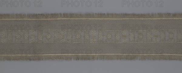A so-called Saxon lace belt, lace, belts, clothing accessories, men's clothing, clothing, fashion, provenance unknown. The central part is a continuous belt with a geometric ornament; among the motifs is a circle containing an hourglass. The side belts of similar width are permanently connected. The entire belt is trimmed with fringe. 17th–18th century, Poland. Lace, clothing accessories, clothing. Height 270 cm, width 25 cm., A horizontal strip of fabric with a central band featuring a repeating geometric lace pattern in muted gray and tan tones, flanked above and below by textured mesh-like panels in similar gray and taupe shades, and edged on both long sides with a fringe of beige and light brown threads; the background visible above and below the strip is a flat cool gray.