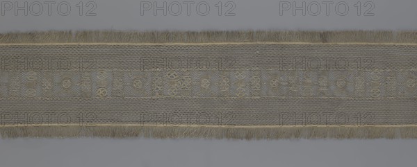 A so-called Saxon lace belt, lace belt accessory for men's clothing. The central part is a continuous belt with a geometric ornament; among the motifs is a circle containing an hourglass. The side belts of similar width are permanently connected. The entire belt is trimmed with fringe. 17th–18th century, Poland. Lace, clothing accessory; height 270 cm, width 25 cm., A long horizontal textile band with fringed edges runs across a neutral background; the band shows a central decorative strip flanked by textured panels, all in muted tones of beige, tan, gray, and hints of olive. The fringes at the top and bottom edges are a mix of beige and tan threads. The central strip contains a repeating mosaic of small geometric motifs created by raised stitching in beige and olive against a mottled gray-beige ground. Adjacent panels on either side of the central strip display a fine net-like or lattice texture in pale gray and beige, with subtle variations in thread thickness creating a slightly thr...