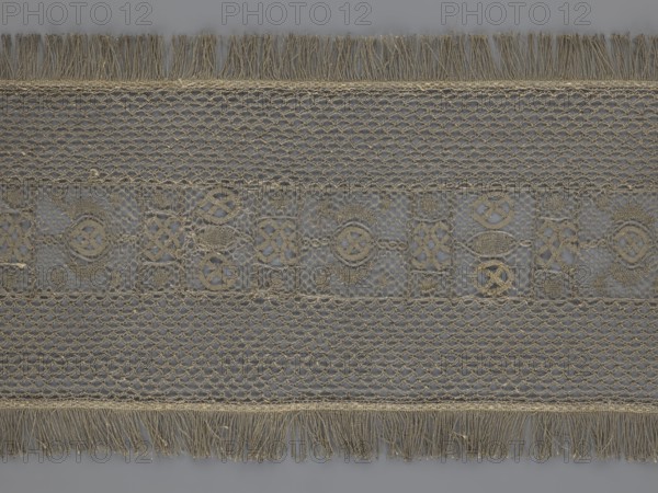 So-called Saxon lace belt; maker, lace belt for men's clothing; 17th–18th century, Poland. Central continuous belt with geometric ornament including a circle containing an hourglass; side belts of similar width permanently connected; entire belt trimmed with fringe. Materials: lace; dimensions: height 270 cm, width 25 cm., A horizontal piece of lace or trim with a repeating decorative pattern and fringed edges, shown flat against a neutral background; the lace has openwork sections with looped and knotted designs forming geometric and circular motifs, alternating with tighter mesh bands, and the top and bottom edges have long tasseled fringes. The visible colors are shades of beige and gray.