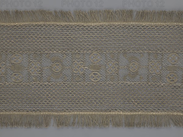 A so-called Saxon lace belt, creator, lace belt men's clothing accessory. The central part is a continuous belt with a geometric ornament, including a circle containing an hourglass motif. Side belts of similar width are permanently connected. The entire belt is trimmed with fringe. 17th–18th century, Poland. Lace; height 270 cm, width 25 cm., A rectangular piece of lace fabric laid flat with a repeating horizontal pattern, featuring a central band with ornate geometric motifs and surrounding bands of open net-like stitching; fringed edges run along the top and bottom. The visible colors are shades of beige and tan for the lace against a muted gray background, with subtle variations where the threads overlap. The lace shows textured braided borders, hexagonal and diamond openwork, and circular and interlaced decorative shapes in the central area, all in the same beige-tan tones. The fringe consists of loose hanging threads in beige and tan, and the overall surface displays fine threadw...