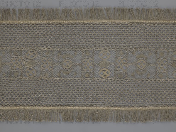 A so-called Saxon lace belt, lace, belts, clothing accessories, men's clothing, clothing, fashion, deposit provenance. The central part is a continuous belt with a geometric ornament; among the motifs there is a circle containing an hourglass. The side belts of similar width are permanently connected. The entire belt is trimmed with fringe. 17th/18th century, Poland. Lace, clothing accessories, clothing. Height 270 cm, width 25 cm., A wide horizontal strip of lace with a repeating openwork pattern in beige and gray tones, featuring a central band of decorative motifs set against a translucent gray background, flanked by two bands of netlike lattice, with fringed edges at the top and bottom made of loose beige threads.